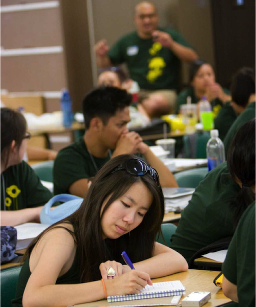 young woman writing at desk in classroom