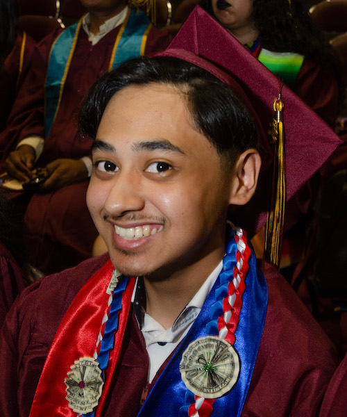 young man in grad cap, smiling with folded dollar necklace