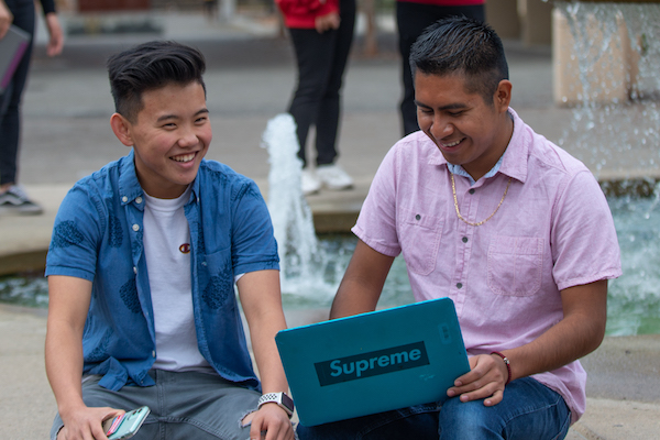 two students with laptop in front of fountain