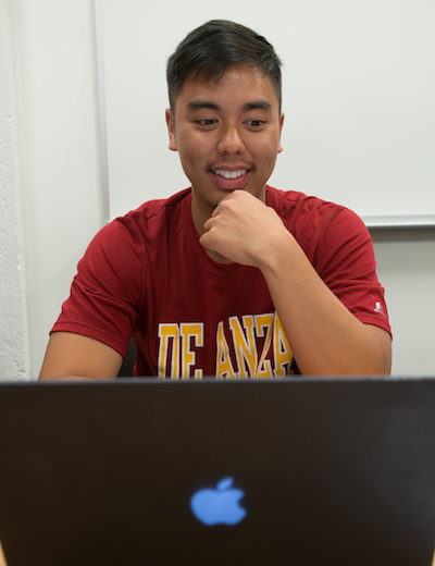 Young man in De Anza shirt sitting in front of laptop computer