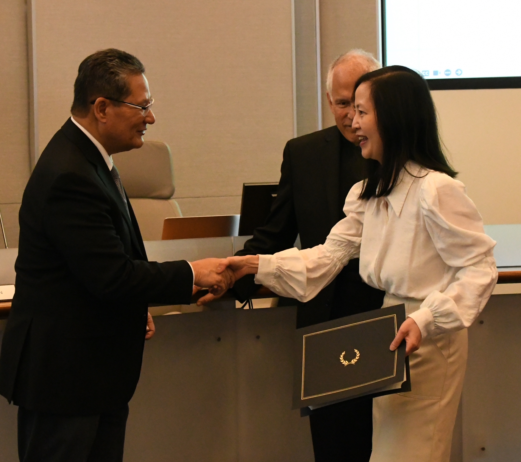 Chancellor Lambert shaking hands with Catherina Wong as Trustee Landsberger looks on