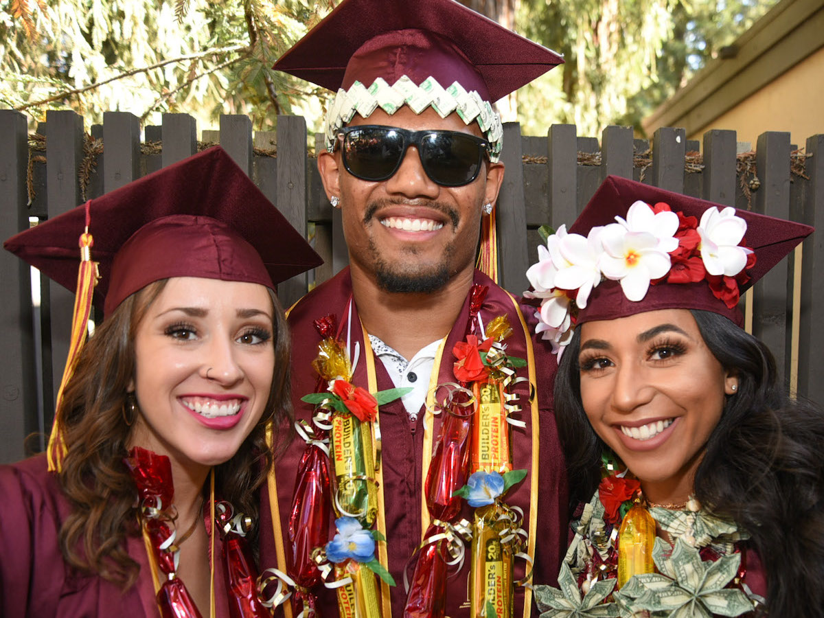 male grad in sunglasses and two women grads, one with flowers