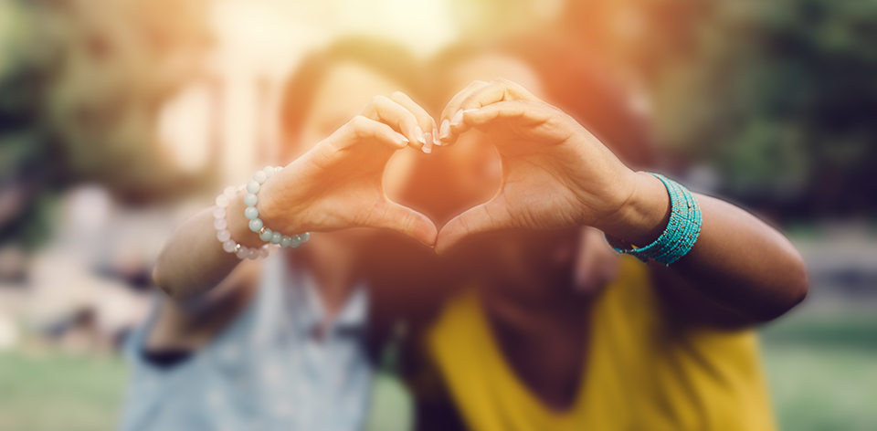 two girls holding out hands to make a heart symbol