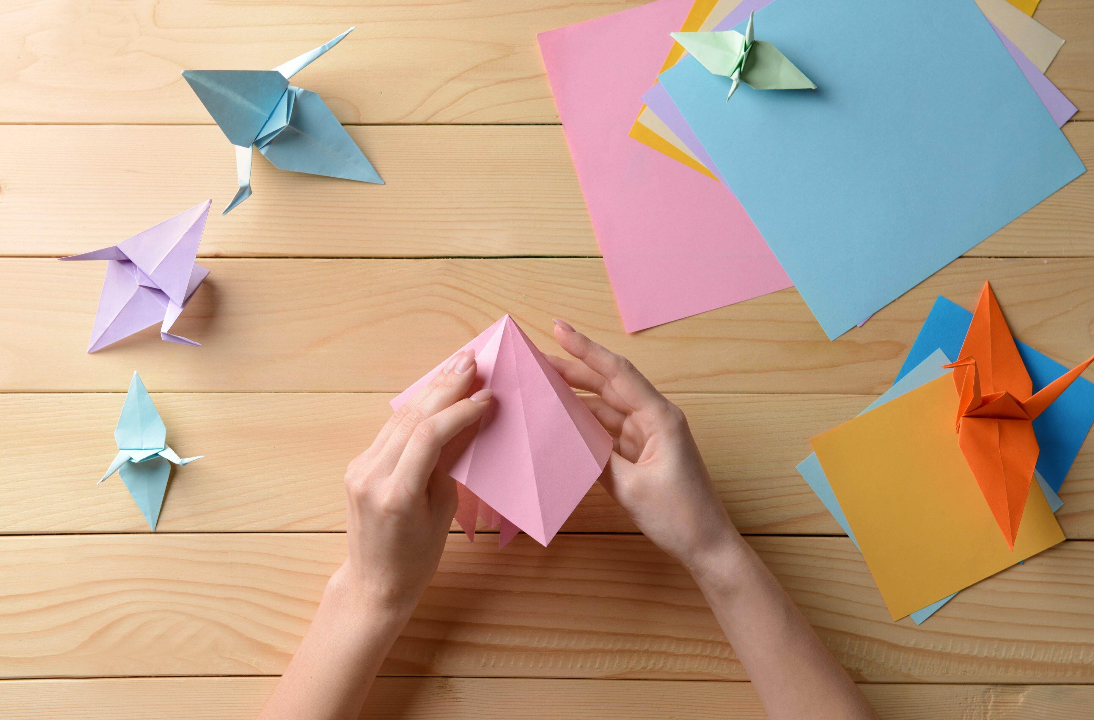hands folding colored paper for origami