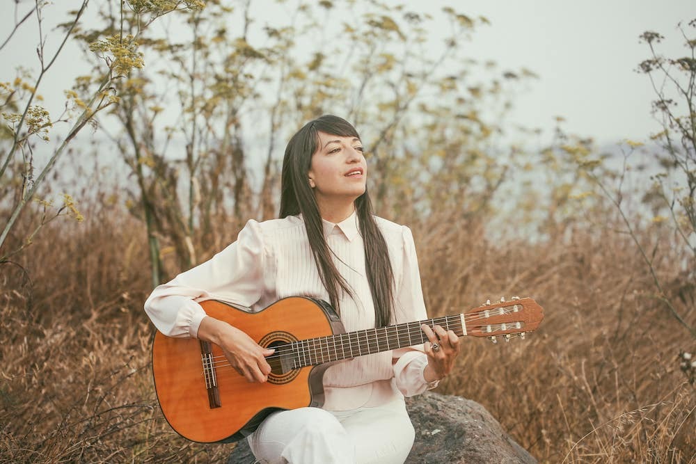 Diana Gameros: woman in white playing guitar outdoors