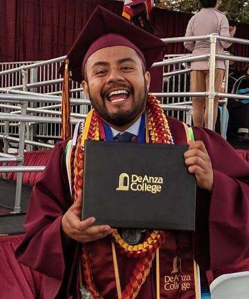 male student in cap and gown looking excited while holding diploma cover